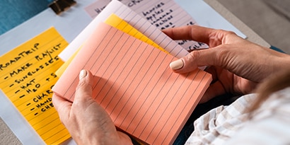 Hands holding a stack of 4 in x 6 in Post-it® Super Sticky Notes, in various colors.